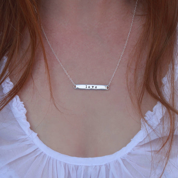 Sterling Silver hand-stamped 'love' necklace on neck.
