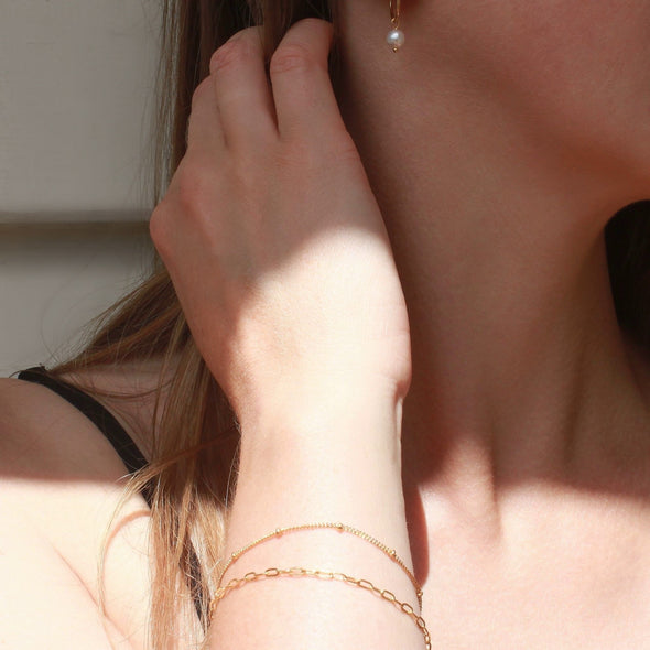 Gold chain bracelets on wrist and pearl earrings