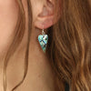 Paua shell heart earrings on the ear.