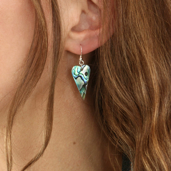 Paua shell heart earrings on the ear.